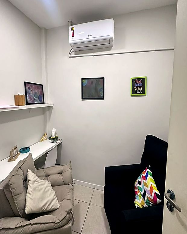 Sala de atendimento da clínica, com duas poltronas, escrivaninha e quadros na parede.
