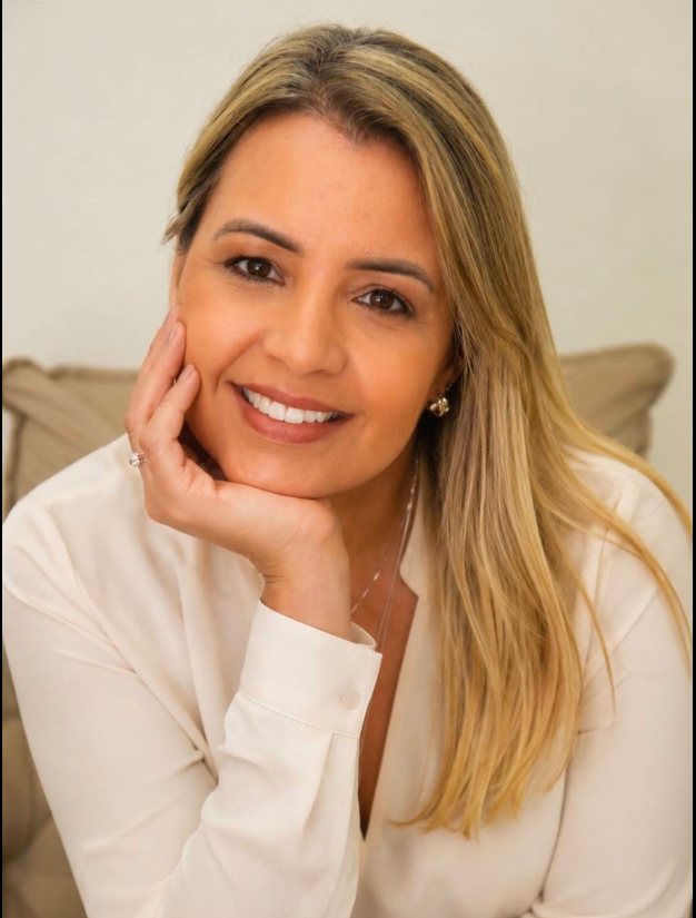 Daniela Assunção, psicóloga, sorrindo com a mão apoiada no rosto.